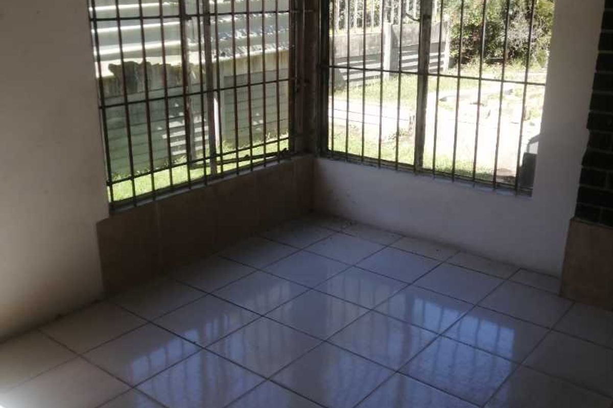 A sunlit, tiled interior space featuring large windows secured with metal burglar bars, offering a view of the garden area.