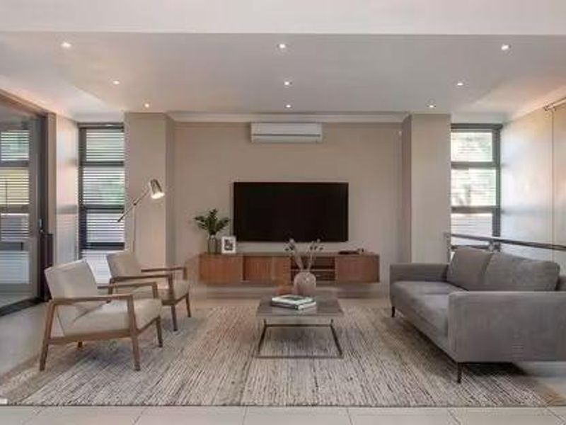 Modern, well-lit living room featuring tiled floors, recessed lighting, a split-system air conditioner, and a sleek staircase with stainless steel railings.