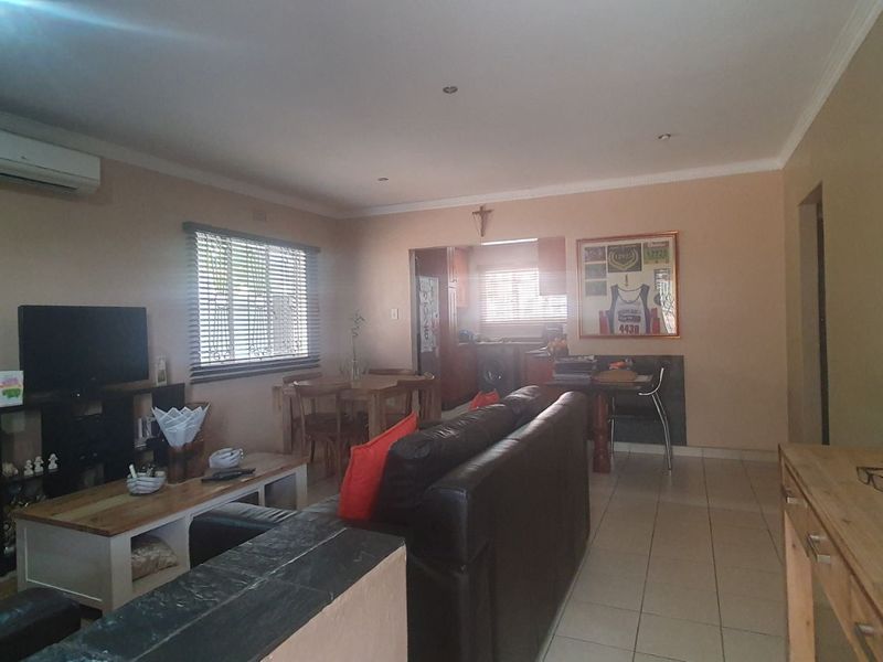 Open plan living area featuring tiled flooring, recessed lighting, and an integrated air conditioning unit, connecting to a kitchen space.