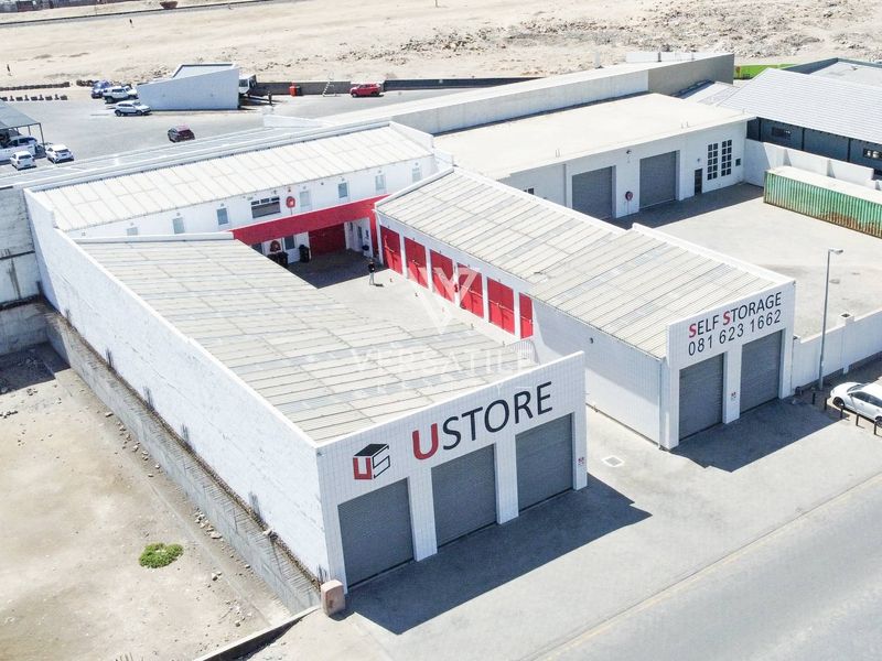 Aerial view of a commercial self-storage facility featuring multiple roller shutter doors, metal roofing, and paved access areas.
