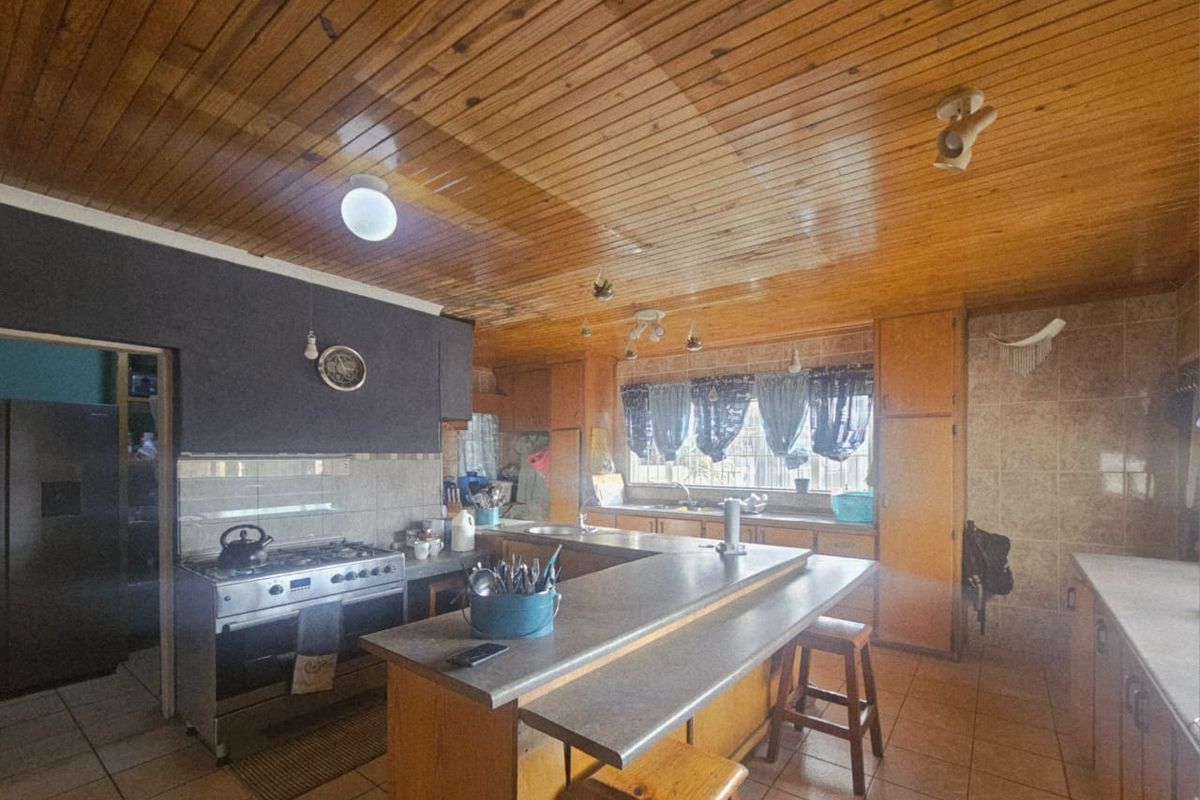 Spacious kitchen featuring a central breakfast bar, built-in cabinetry, tiled flooring, and a distinctive timber-paneled ceiling.