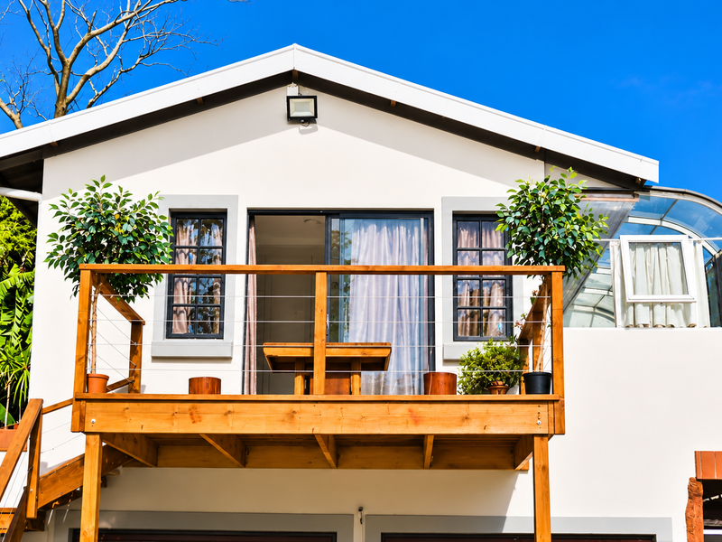 Rear view of the property featuring a raised wooden deck with staircase access, sliding glass doors, and a unique curved glass roof section.
