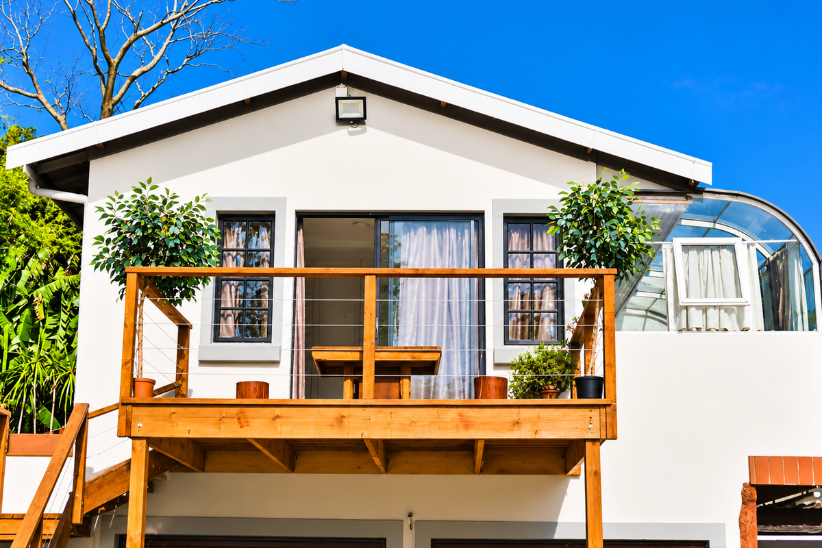 Rear view of the property featuring a raised wooden deck with staircase access, sliding glass doors, and a unique curved glass roof section.