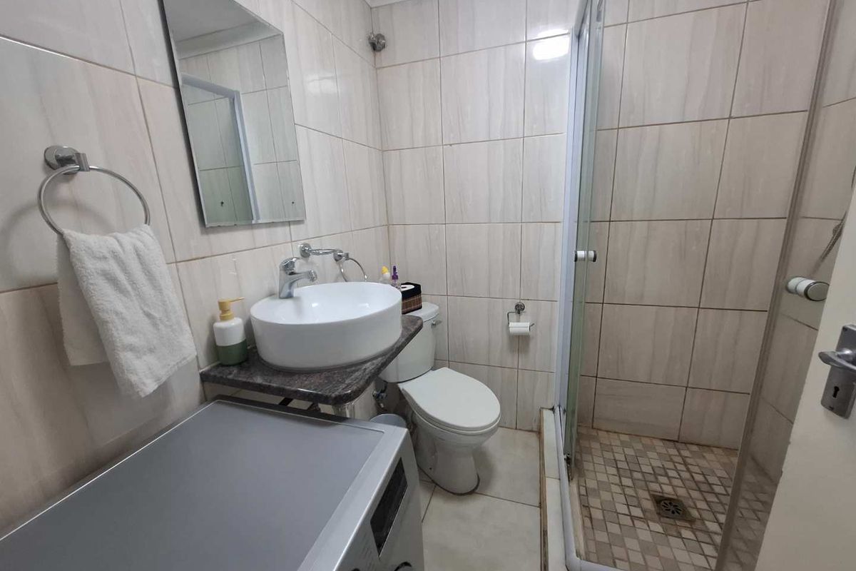 Compact bathroom featuring a glass-enclosed shower, vessel sink vanity, and toilet with neutral wall tiling.