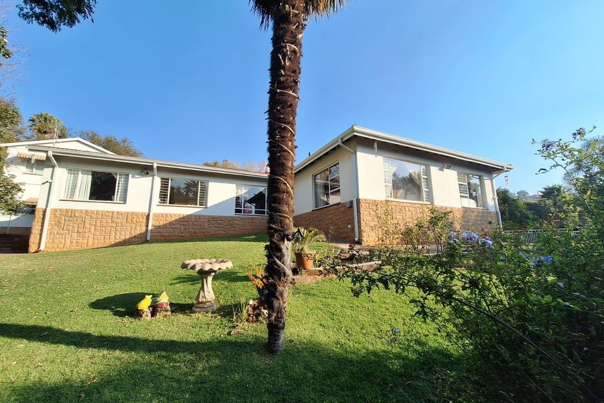 Rear view of the house featuring a well-maintained lawn, stone-clad base, and plastered exterior walls with large windows.