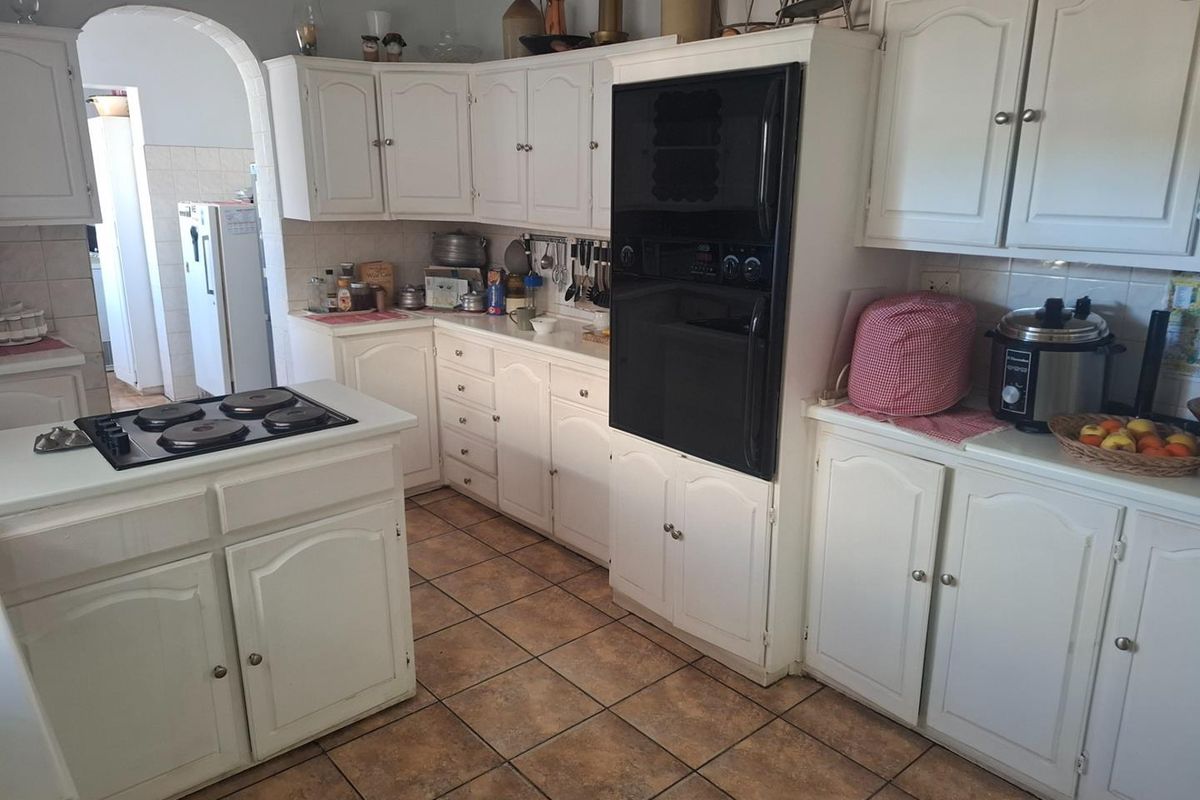 A functional kitchen featuring white cabinetry, a built-in oven, an electric hob, and tiled flooring, with an arched doorway leading to an adjacent utility area.