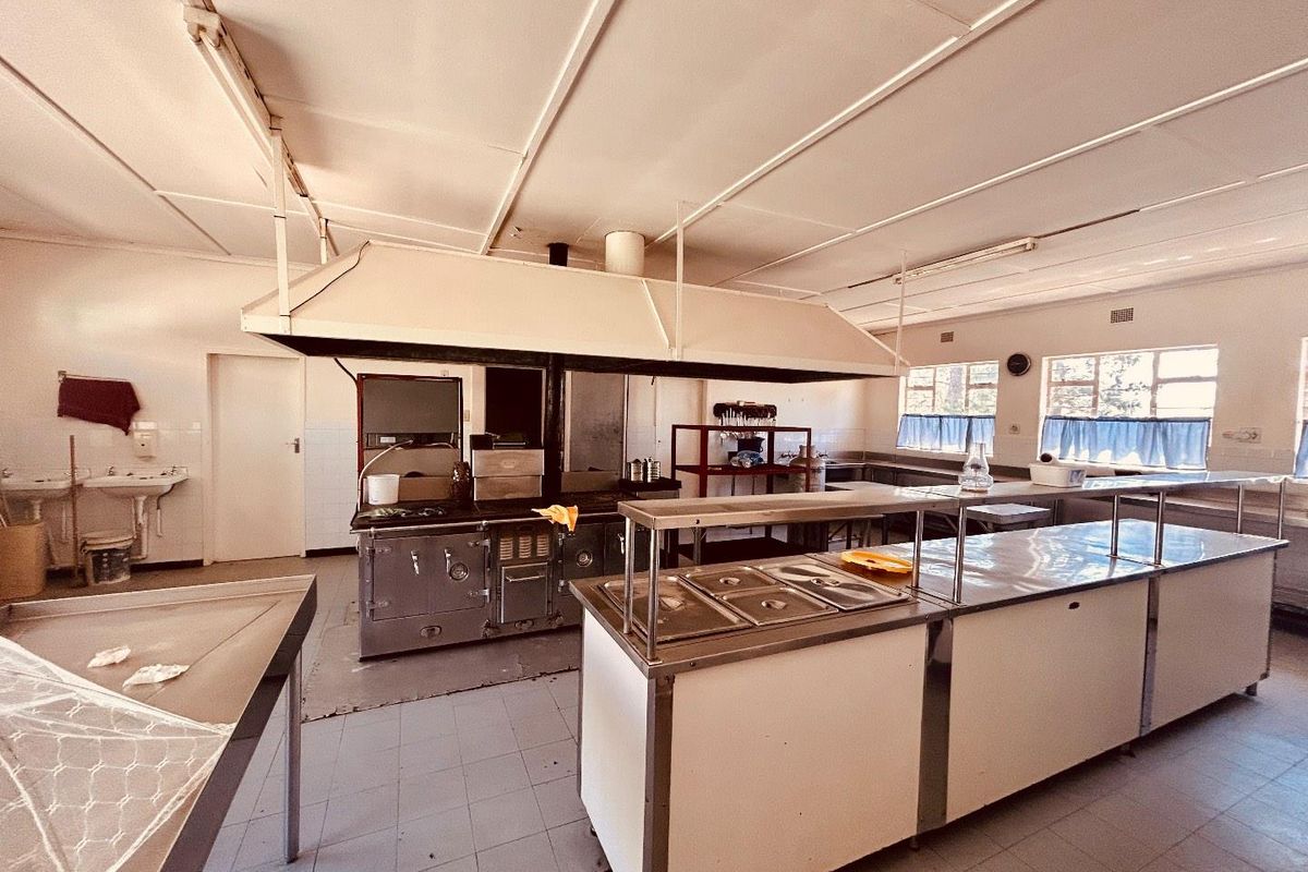 Commercial-style kitchen featuring stainless steel prep counters, a large central extractor hood, and industrial cooking equipment in a functional, dated layout.