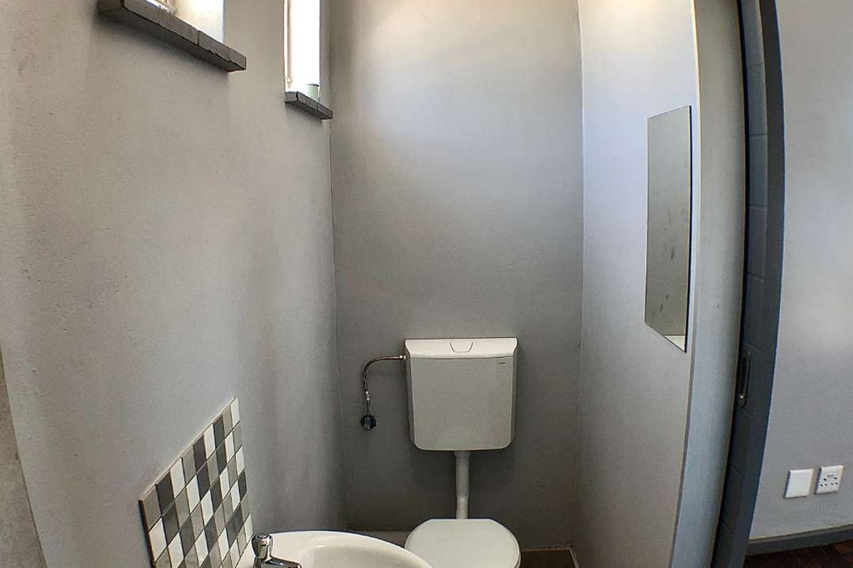 A compact guest bathroom featuring a white toilet, wall-mounted washbasin with a tiled splashback, and a sliding door entrance.