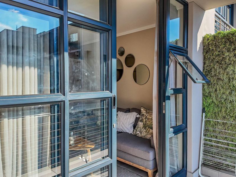 A modern balcony featuring dark aluminium-framed glass doors and a lush vertical garden wall, providing a seamless transition to the interior living space.