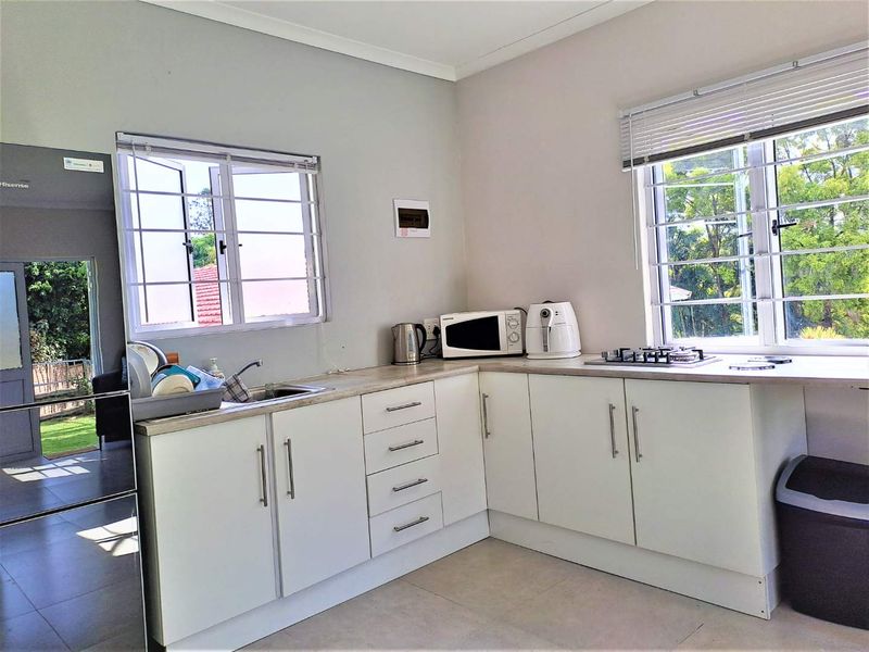 A functional kitchen featuring white cabinetry, laminate countertops, a gas hob, and large windows with security bars, offering a bright and practical workspace.