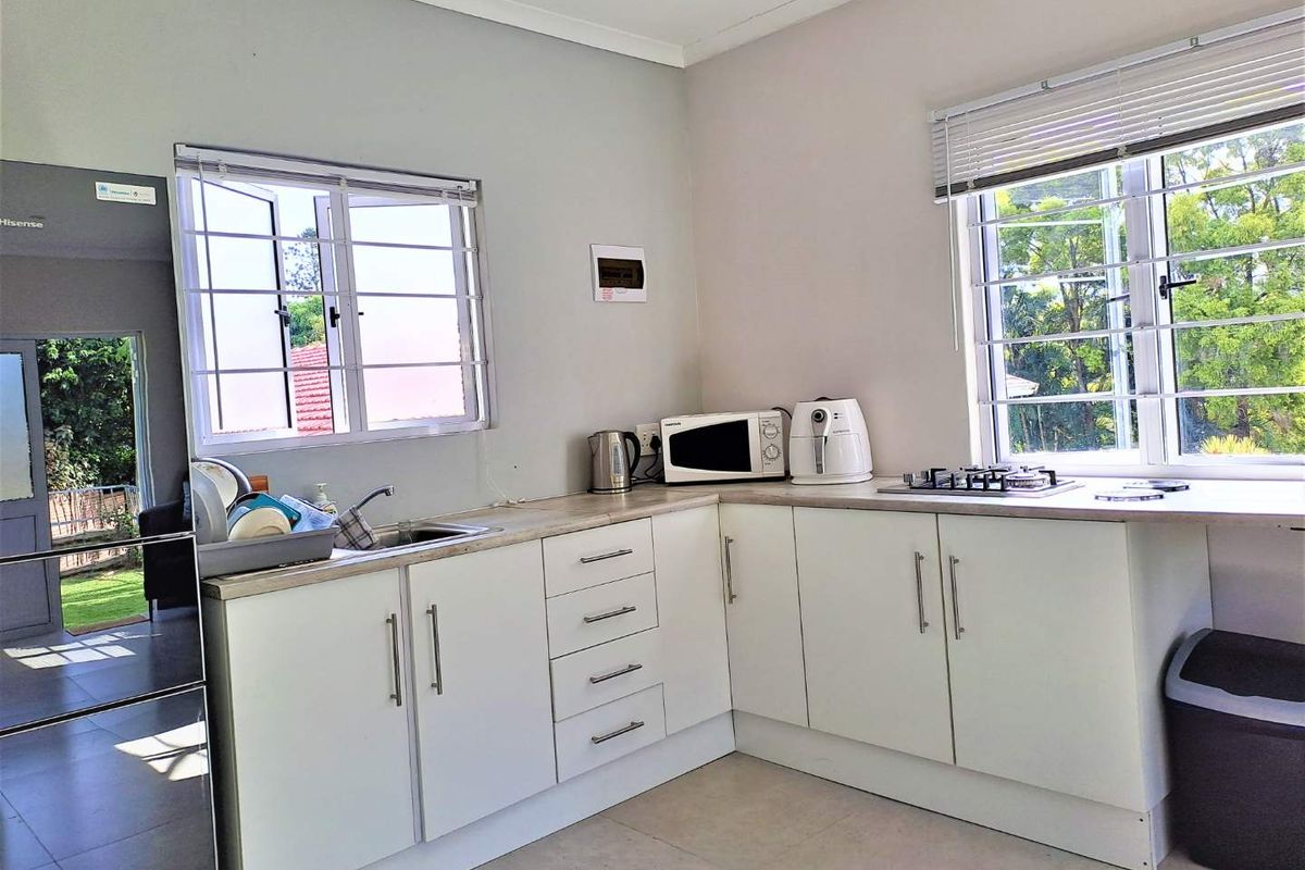 A functional kitchen featuring white cabinetry, laminate countertops, a gas hob, and large windows with security bars, offering a bright and practical workspace.