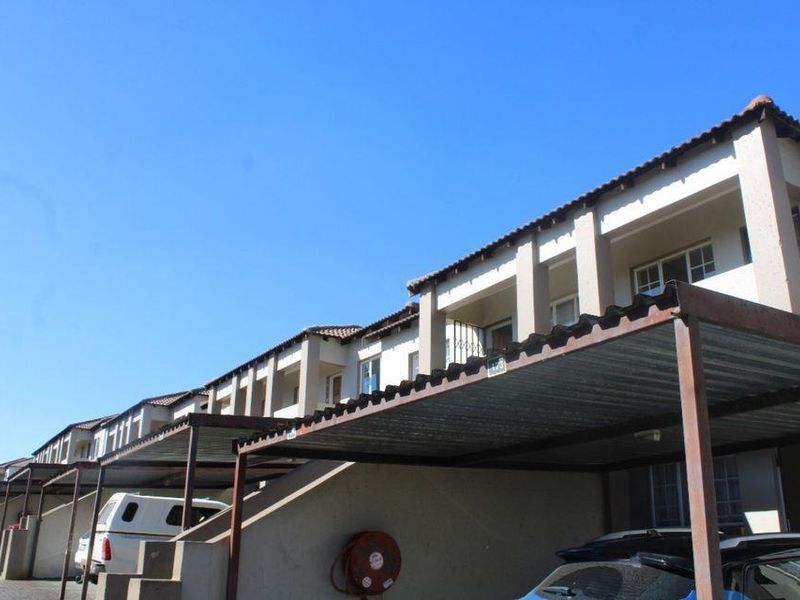 Exterior view of a townhouse complex featuring covered carports, tiled roofing, and upper-level balconies.