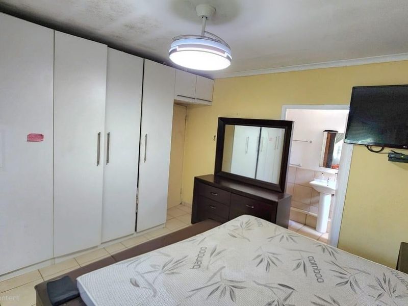 Bedroom featuring built-in cupboards, tiled flooring, and an en-suite bathroom. The room shows signs of ceiling water damage and requires cosmetic attention.