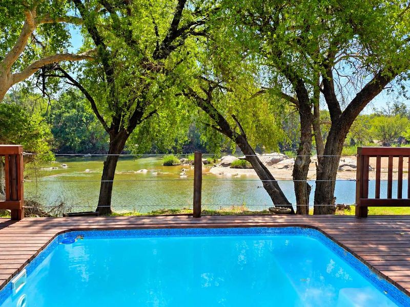 A well-maintained swimming pool set within a timber deck, featuring a wooden balustrade and scenic river views framed by mature trees.
