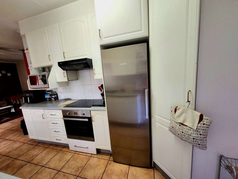 A functional kitchen featuring white cabinetry, tiled backsplash, and integrated appliances including an oven, hob, and extractor fan.