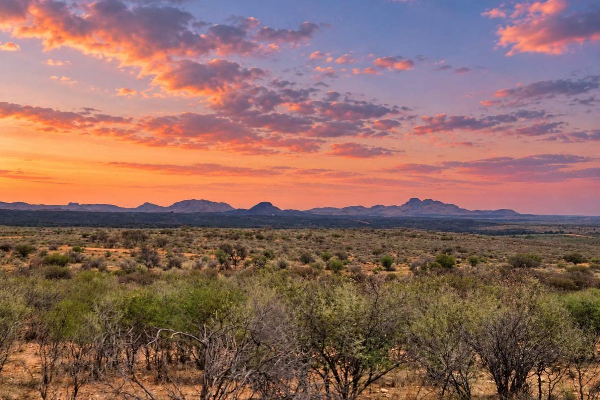 A scenic landscape view of the vacant residential land featuring natural vegetation and distant mountain ranges under a vibrant sunset sky.