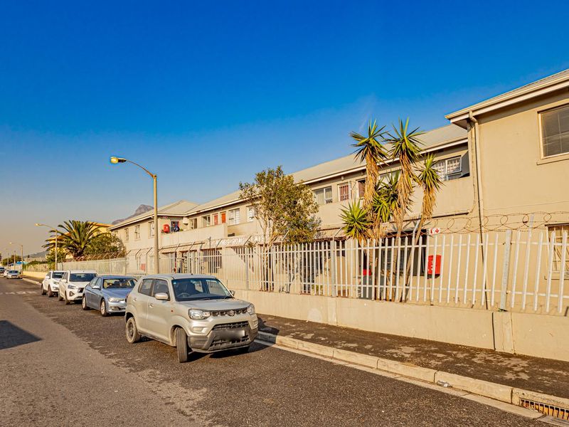 Street-level view of the apartment complex facade featuring security fencing, razor wire, and multi-story residential units with metal window frames.