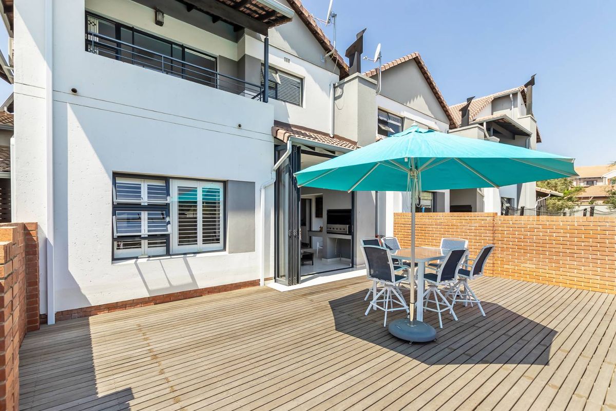 A spacious rear patio featuring timber decking, brick boundary walls, and large folding doors providing seamless access to the interior living space.