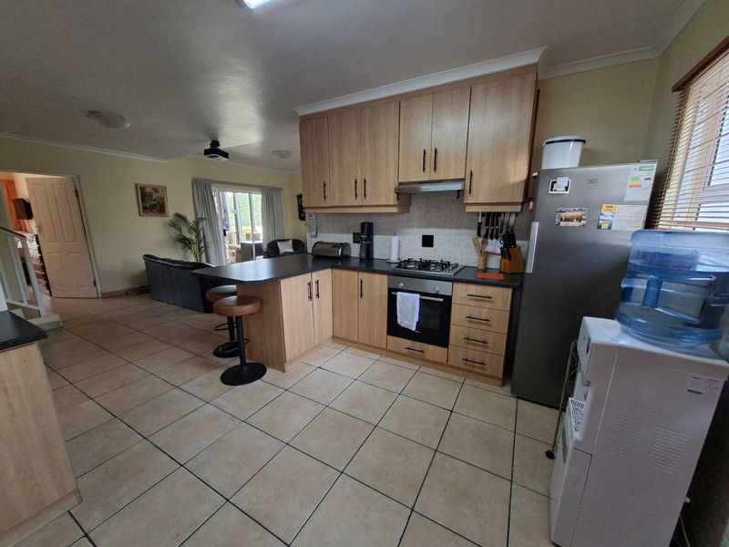 Open-plan kitchen and living area featuring light wood cabinetry, gas hob, built-in oven, and tiled flooring throughout.