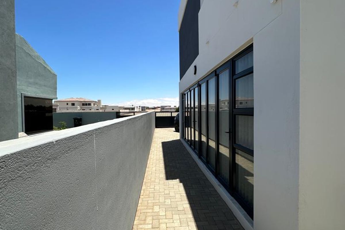 A side exterior walkway featuring paved flooring and large glass sliding doors providing access to the interior of the modern property.