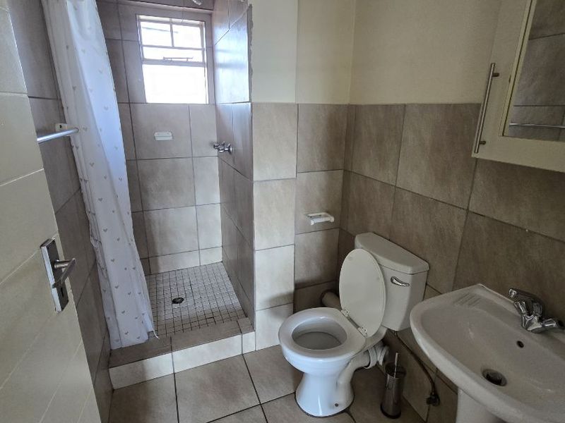 A functional bathroom featuring a pedestal basin, toilet, and a tiled shower enclosure with a curtain rail.