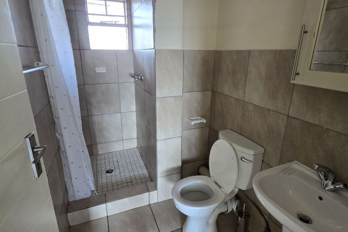 A functional bathroom featuring a pedestal basin, toilet, and a tiled shower enclosure with a curtain rail.