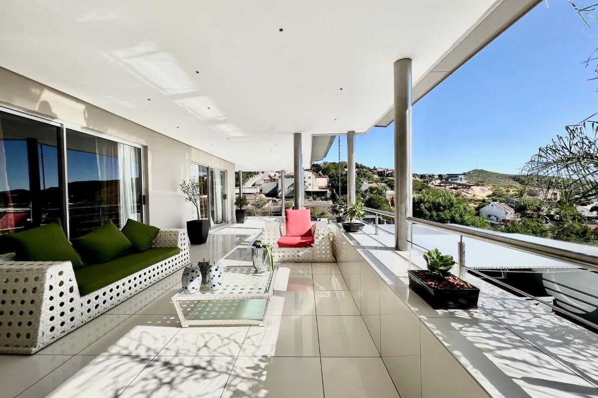 Spacious covered balcony featuring tiled flooring, stainless steel support columns, and a glass balustrade, offering expansive elevated views.