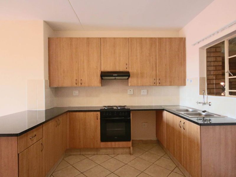 A functional kitchen featuring laminate cabinetry, granite countertops, a built-in oven with hob, and a double sink with tiled backsplash.