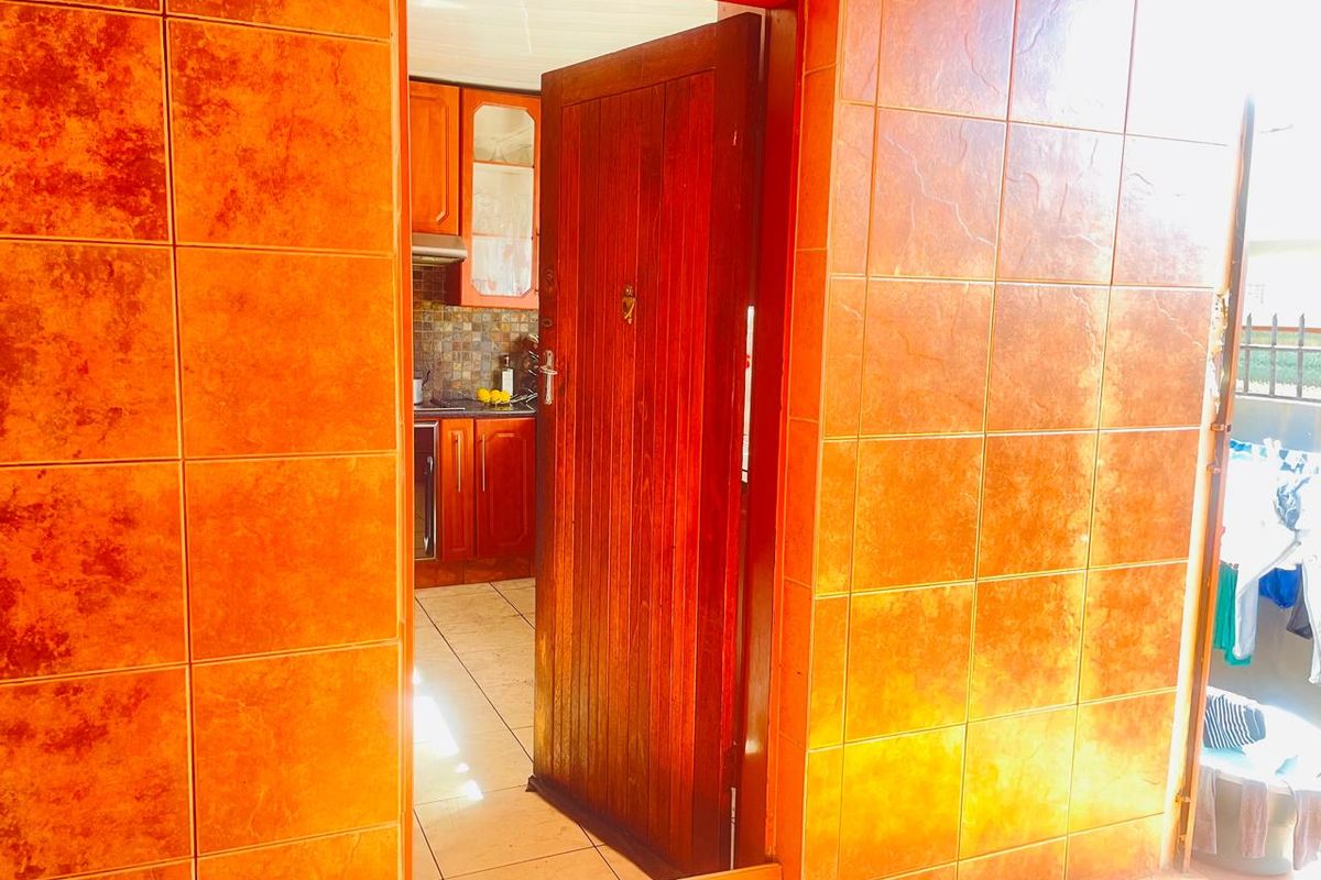 A view through a wooden doorway into a kitchen featuring timber cabinetry and tiled surfaces.