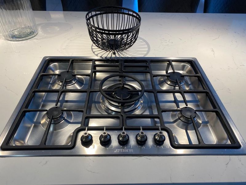 A modern stainless steel five-burner gas cooktop integrated into a white stone kitchen island countertop.