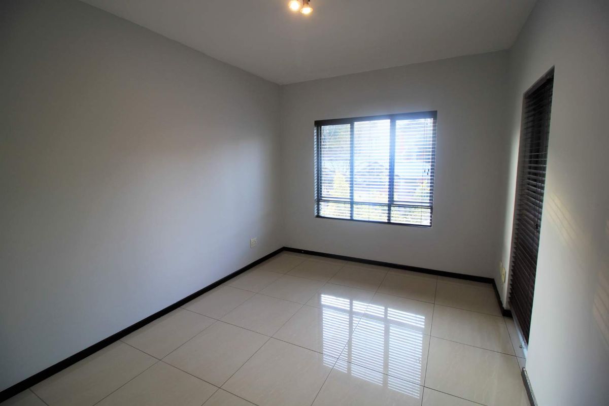 A bright, empty bedroom featuring neutral tiled flooring, clean walls, and fitted window blinds, offering a versatile space ready for personalization.