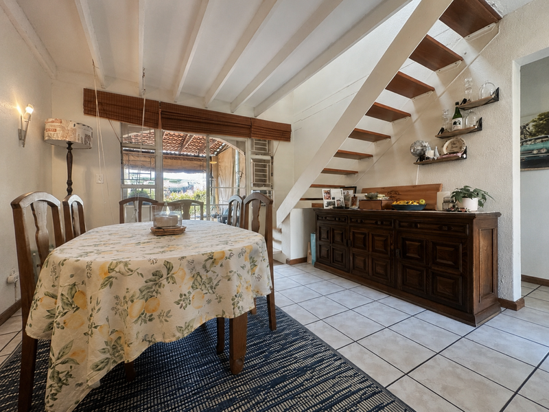 Dining area featuring exposed ceiling beams, tiled flooring, and an open staircase leading to the upper level with access to an outdoor patio.