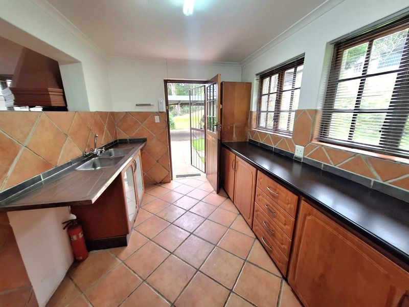 A functional kitchen featuring wooden cabinetry, laminate countertops, double basin sink, and tiled finishes with direct access to the exterior.