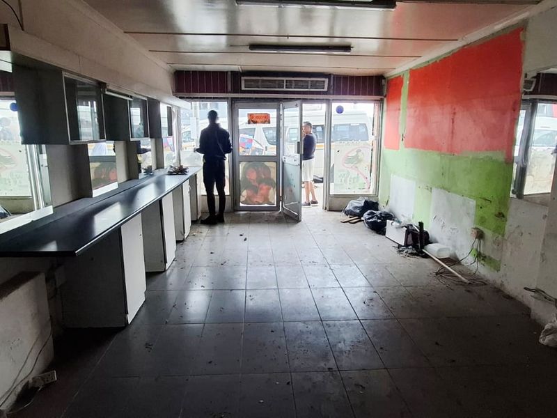 Vacant commercial space featuring tiled flooring, built-in vanity counters with mirrors, and a glass entrance door, requiring cosmetic refurbishment and repairs.