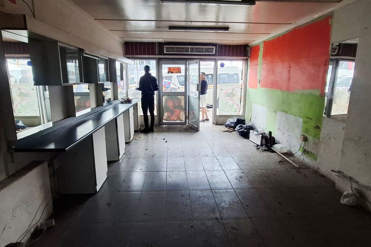 Vacant commercial space featuring tiled flooring, built-in vanity counters with mirrors, and a glass entrance door, requiring cosmetic refurbishment and repairs.