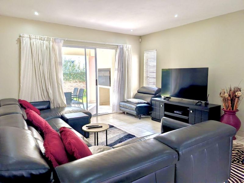 A well-lit living room featuring tiled flooring, recessed downlights, and a large sliding glass door providing access to the outdoor patio area.