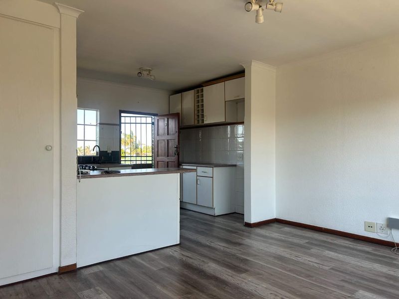 Open plan kitchen and living area featuring laminate flooring, built-in cabinetry, and a breakfast bar, offering a functional layout ready for modern updates.