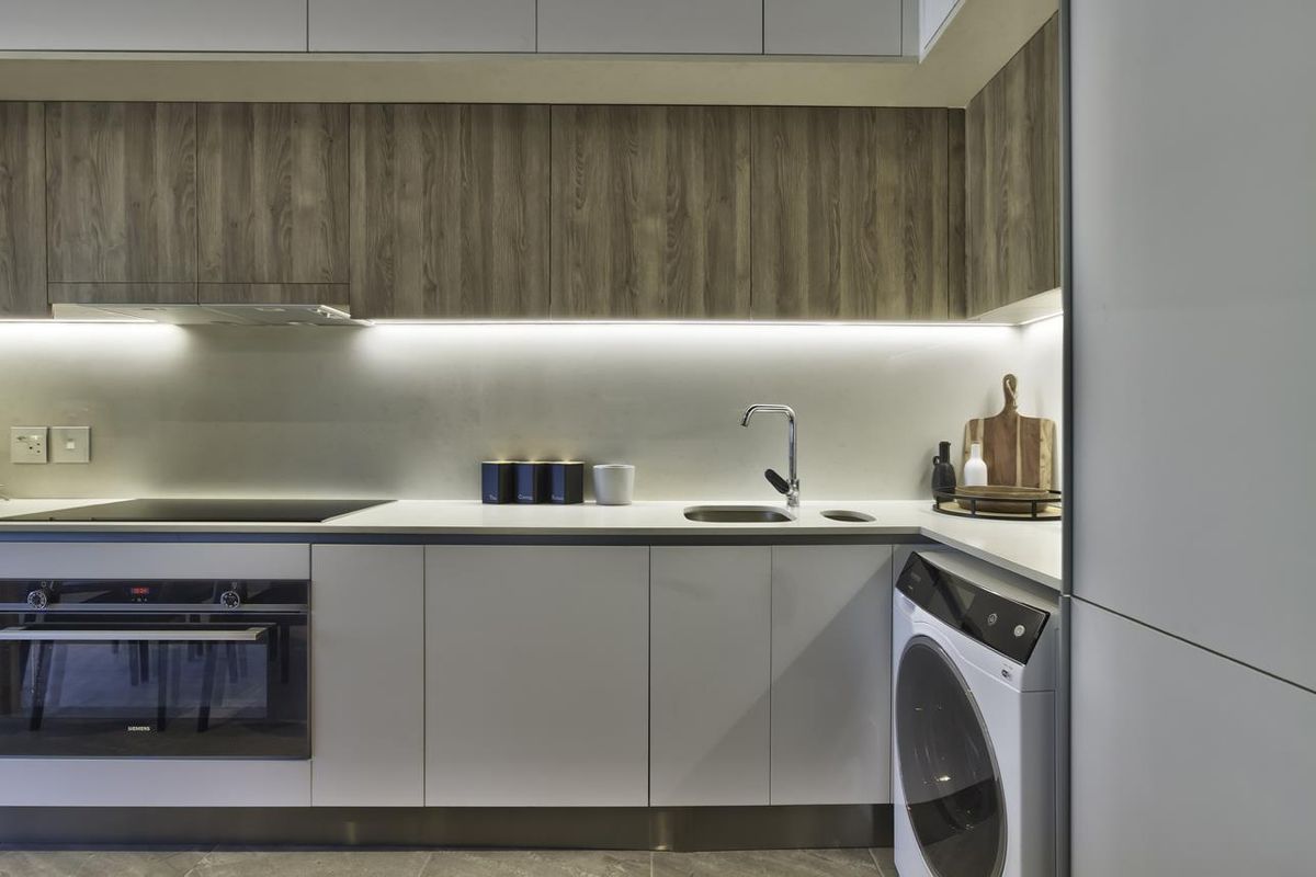 Modern kitchen featuring sleek handleless cabinetry, integrated Siemens oven, induction hob, stone countertops, and an integrated washing machine with ambient under-cabinet lighting.