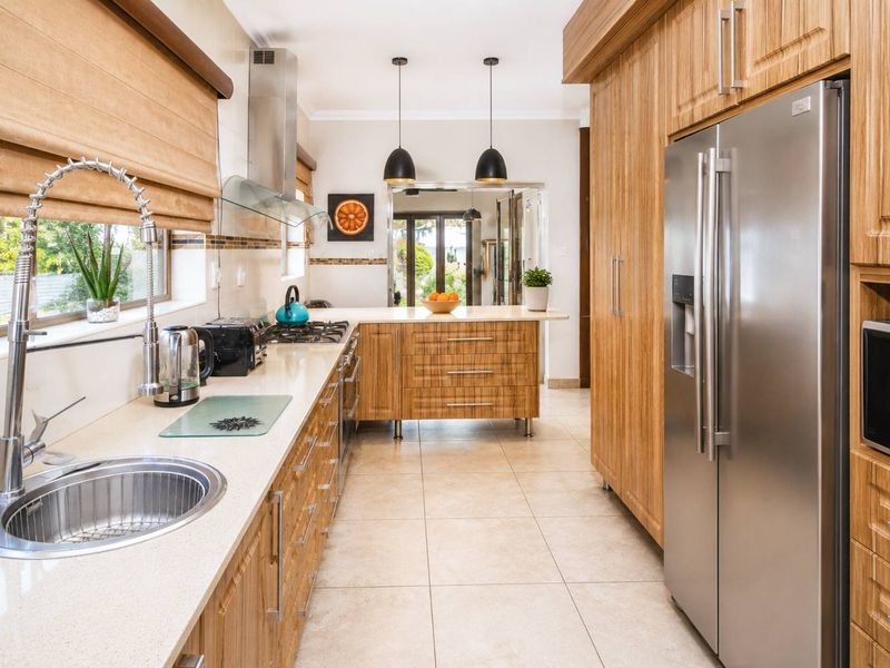 Modern kitchen featuring wood-grain cabinetry, stone countertops, stainless steel appliances, and tiled flooring, with a functional layout and pendant lighting.