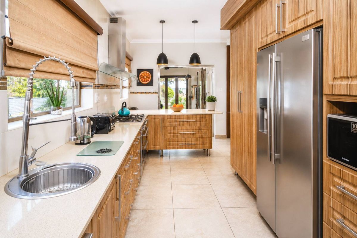 Modern kitchen featuring wood-grain cabinetry, stone countertops, stainless steel appliances, and tiled flooring, with a functional layout and pendant lighting.
