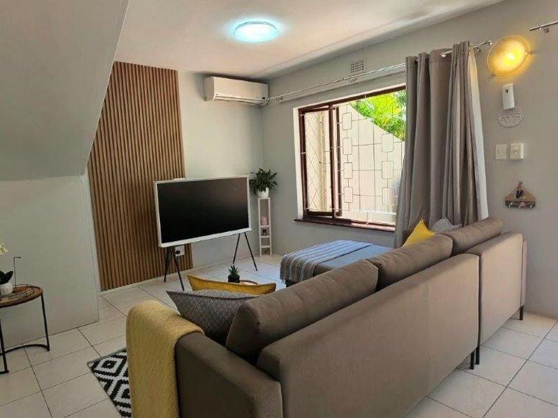 A bright living room featuring tiled flooring, a split-system air conditioner, and decorative slatted wood wall paneling with direct access to an outdoor area.