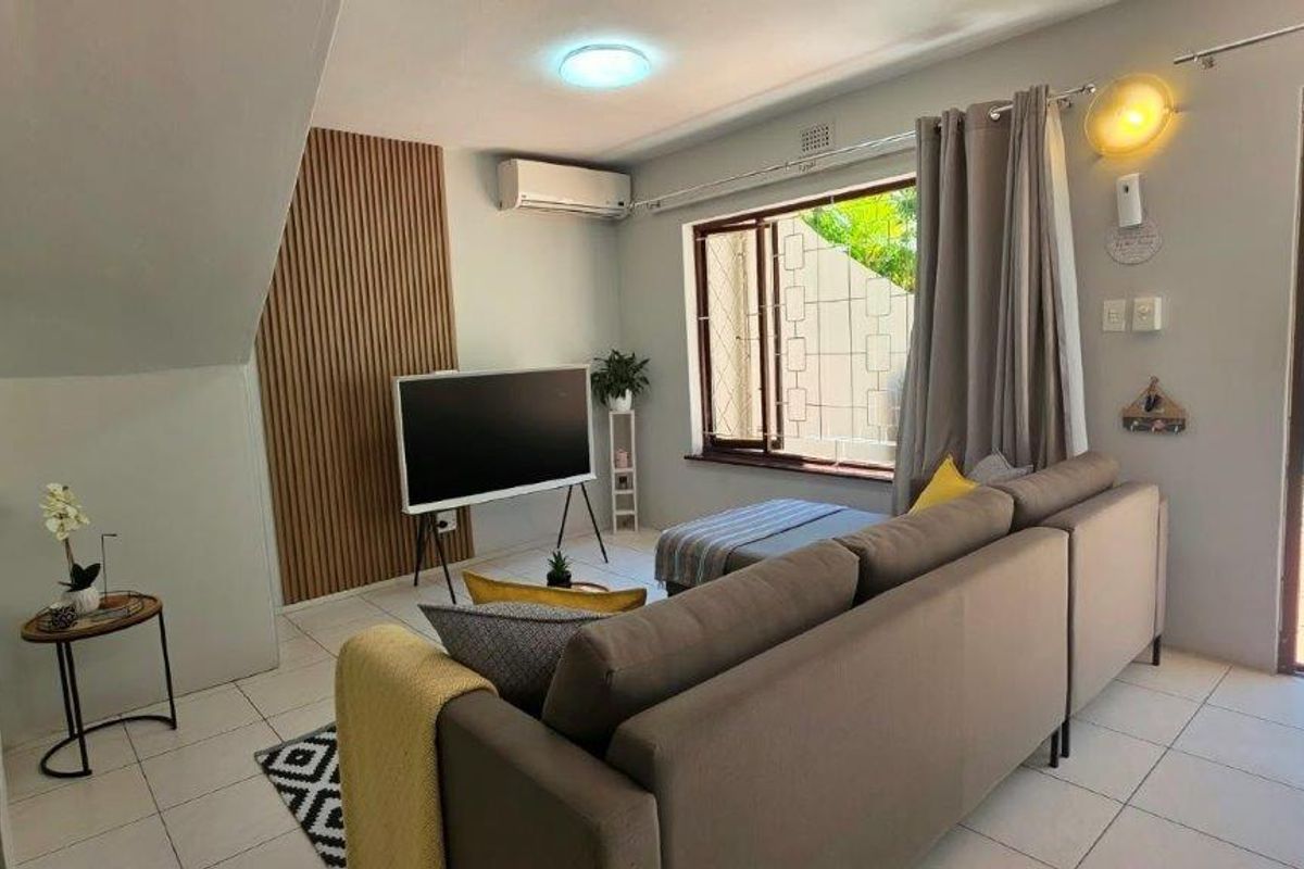 A bright living room featuring tiled flooring, a split-system air conditioner, and decorative slatted wood wall paneling with direct access to an outdoor area.