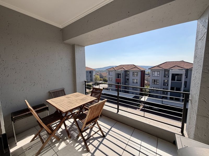 A covered balcony featuring tiled flooring and a metal balustrade, offering an elevated view of the surrounding apartment complex.