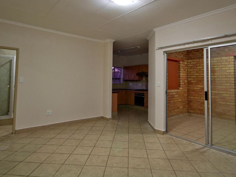 Open plan living area featuring tiled floors, an adjacent kitchen with built-in cabinetry, and a sliding door leading to an enclosed brick patio space.