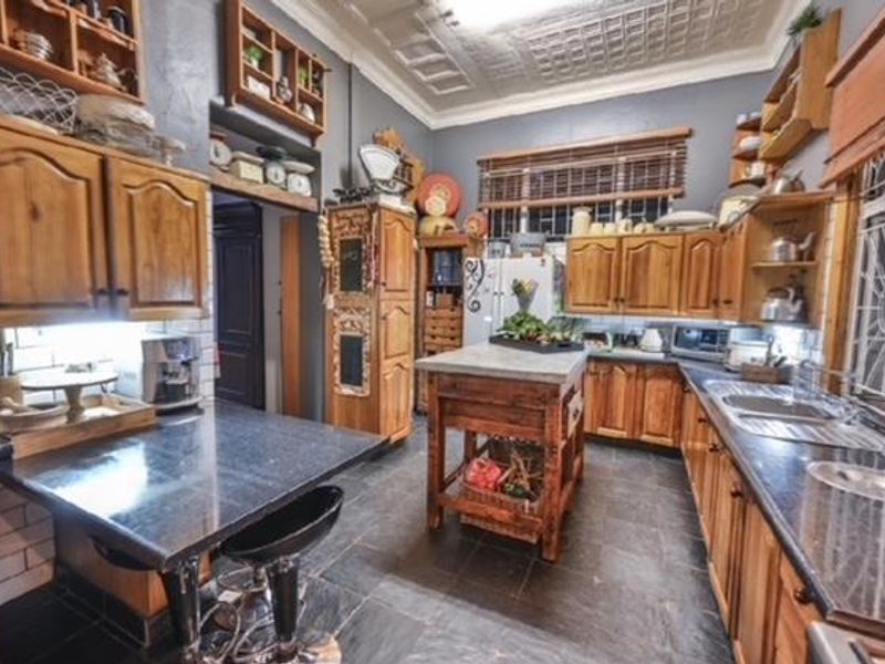 A rustic-style kitchen featuring extensive wooden cabinetry, stone countertops, a double basin sink, and a distinctive pressed metal ceiling.
