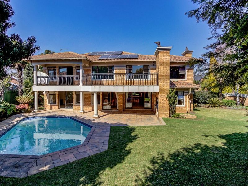 Spacious rear exterior featuring a swimming pool, paved patio area, upper-level balcony, and well-maintained garden with solar panels installed on the roof.