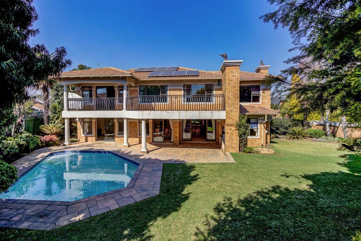 Spacious rear exterior featuring a swimming pool, paved patio area, upper-level balcony, and well-maintained garden with solar panels installed on the roof.