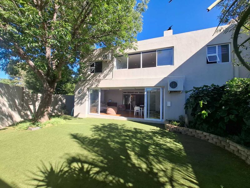 Rear view of the townhouse featuring a private garden with artificial turf, large sliding glass doors, and an upper-level balcony area.