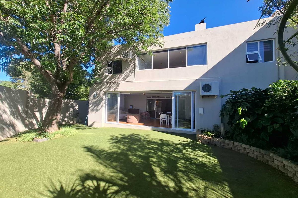 Rear view of the townhouse featuring a private garden with artificial turf, large sliding glass doors, and an upper-level balcony area.