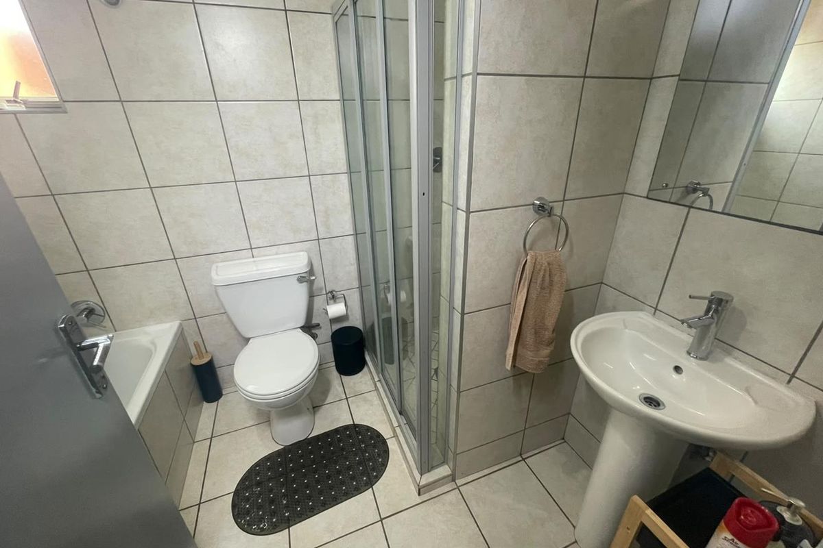 A functional bathroom featuring a pedestal basin, toilet, shower enclosure, and a bathtub with neutral wall and floor tiling.